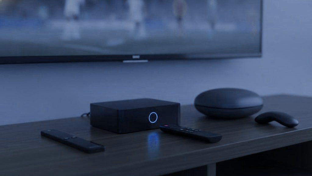 Three streaming devices with their remotes on a TV console: a streaming stick, a set-top box and a round streaming box