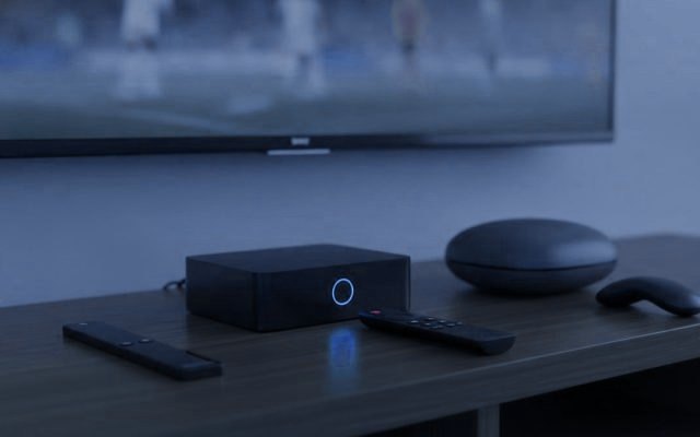 Three streaming devices with their remotes on a TV console: a streaming stick, a set-top box and a round streaming box