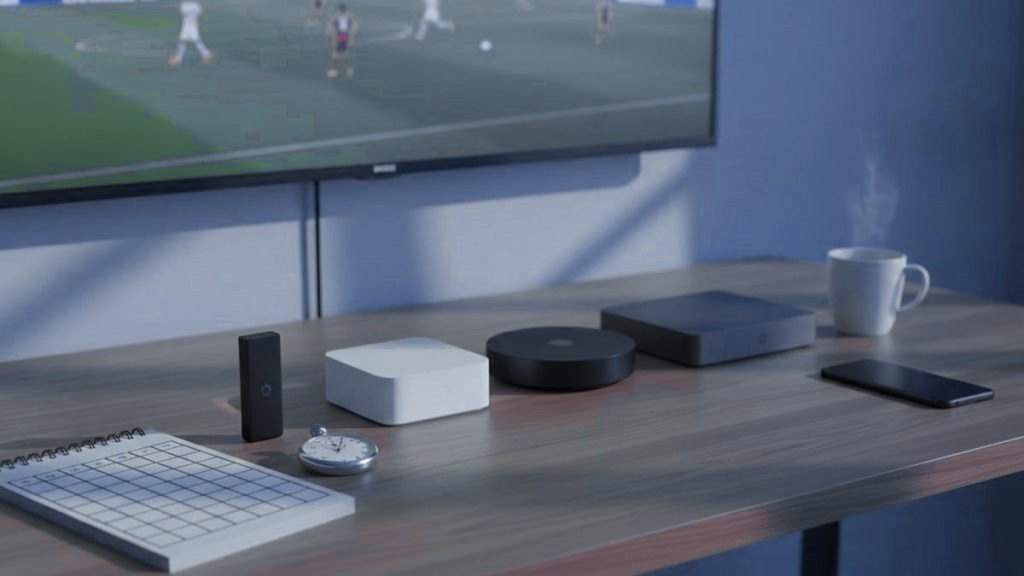 A notebook with a scoring grid, a stopwatch and several streaming devices laid out in front of a TV during a live match